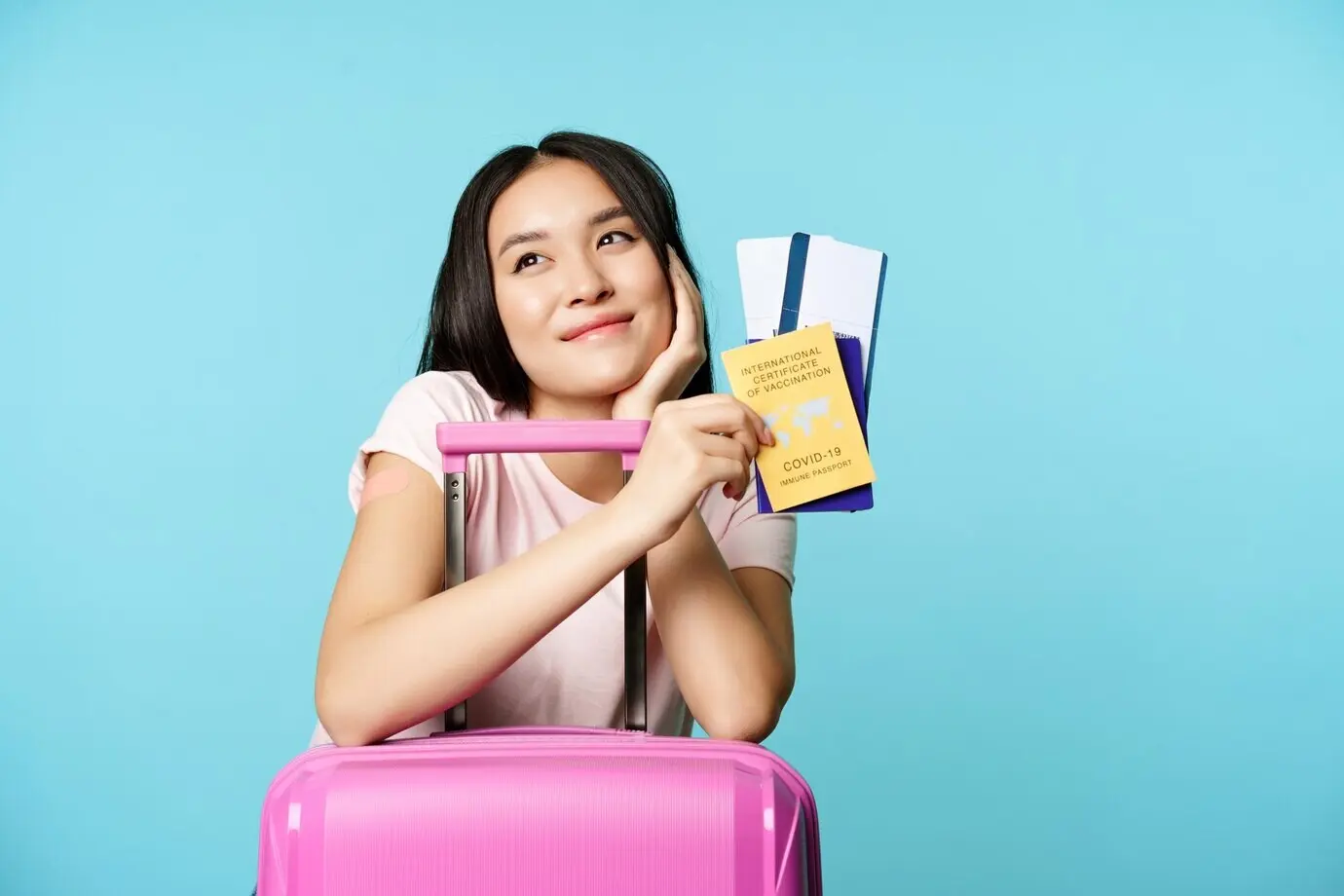 Träumerischer asiatischer Tourist, der lächelt und nachdenkt, hält ein internationales COVID-Impfzertifikat, zwei ti…