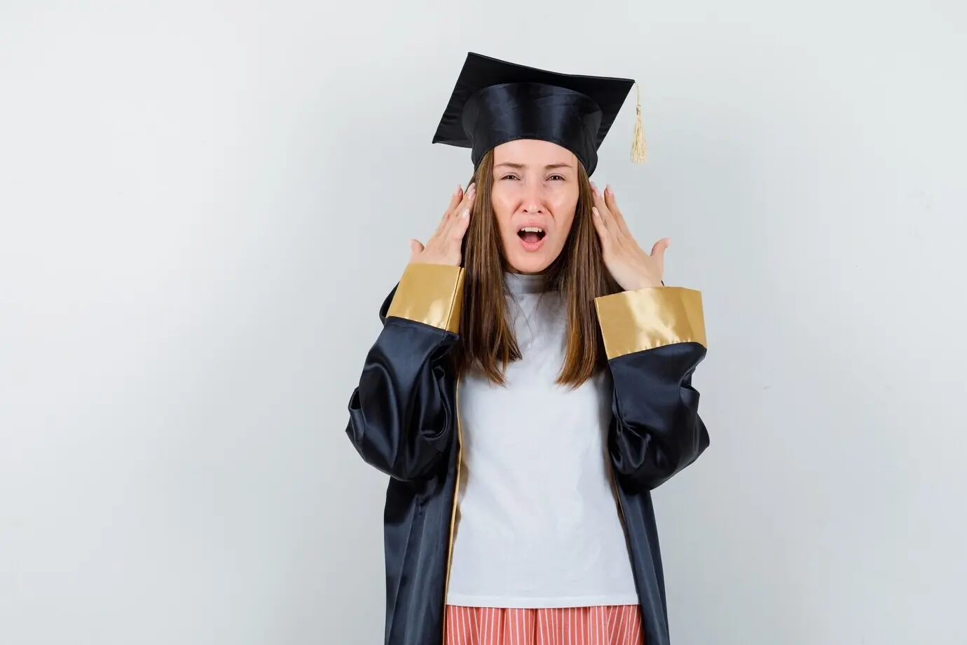 Porträt einer Absolventin, die die erhobenen Hände neben dem Kopf hält, in Freizeitkleidung, Uniform, mit ratlosem Blick, Vorderansicht.